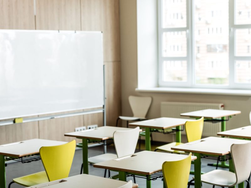 classroom with wooden desks, chairs, window and flipchart