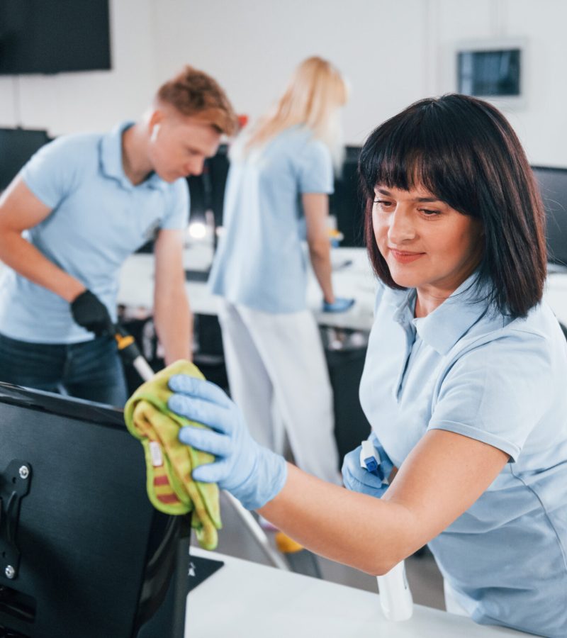 Cleans monitor. Group of workers clean modern office together at daytime.