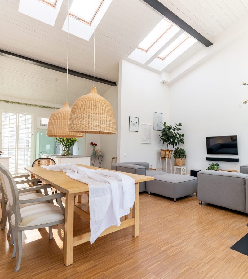 Open space living and dining room interior with flat tv, grey sofa and wooden table with trendy chairs